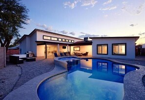 Et moderne hus med swimmingpool, udendørs møbler og en oplyst patio.