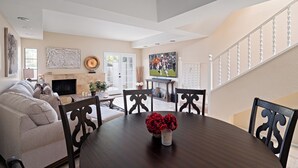 A living room with a dark wooden dining table, beige sofa, and a TV mounted on the wall. - Biltmore Bliss-pool-pickeball-gym-mountain Views (Phoenix)
