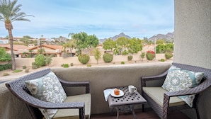 A balcony with wicker chairs, a small table, and a view of a residential area with mountains in the background. - Biltmore Bliss-pool-pickeball-gym-mountain Views (Phoenix)