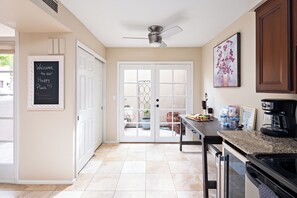 Una cocina con ventilador de techo, un letrero en la pizarra, cafetera y mesa de comedor.