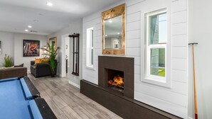 Een moderne woonkamer met een pooltafel, een open haard en een grote spiegel.