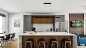 Eine moderne Küche mit einer zentralen Kochinsel, Barhocker, einem eingebauten Kühlschrank und einer Pendelleuchte.