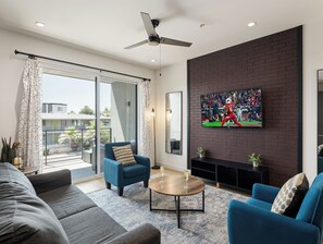 Ein modernes Wohnzimmer mit großem Fernseher, bequemen Sitzgelegenheiten und Blick ins Freie.