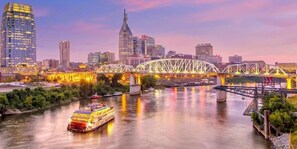A cityscape with a prominent bridge and a riverboat. - Elevate - Modern Luxury - Stunning City Views (Nashville)