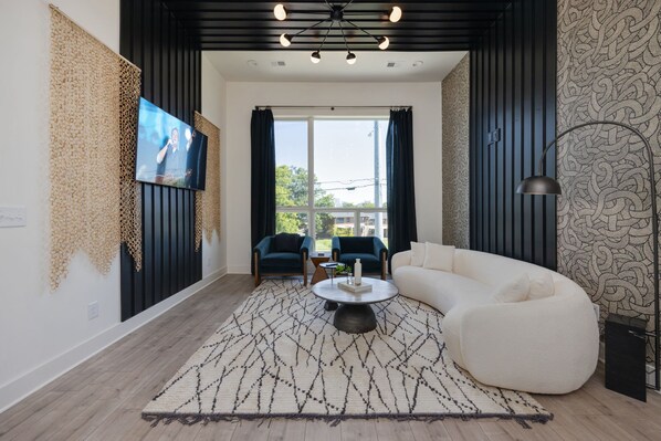 A modern living room with a white sofa, a coffee table, and two blue armchairs. A television is mounted on the wall, and there is a patterned rug on the floor. - Elevate - Modern Luxury - Stunning City Views (Nashville)