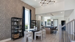 A modern kitchen with a dining area, featuring a marble countertop, white chairs, and a black shelving unit with decorative items. - Elevate - Modern Luxury - Stunning City Views (Nashville)