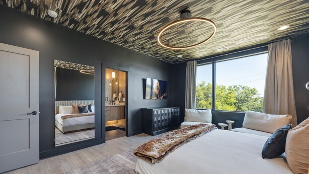 A modern bedroom with a large bed, a walk-in closet, and a view of greenery outside. - Elevate - Modern Luxury - Stunning City Views (Nashville)