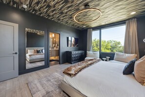A modern bedroom with a large bed, a walk-in closet, and a view of greenery outside. - Elevate - Modern Luxury - Stunning City Views (Nashville)