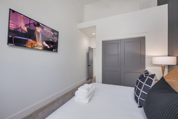 A hotel room with a bed, a TV on the wall, a door, and a lamp. - Elevate - Modern Luxury - Stunning City Views (Nashville)