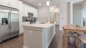 A modern kitchen with stainless steel appliances, a central island with a sink, and a dining area with wooden furniture. - Landing | Amazing 2BD, Clubhouse, Pool (San Antonio)