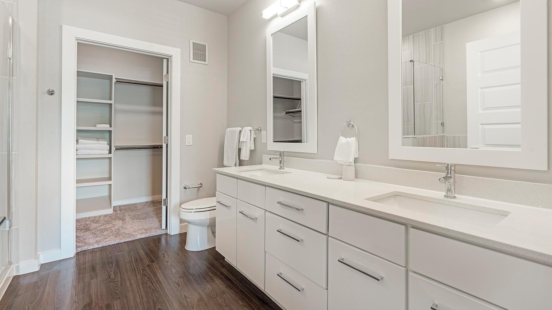 Un baño moderno con vestidor, inodoro y un espejo grande sobre el lavabo.