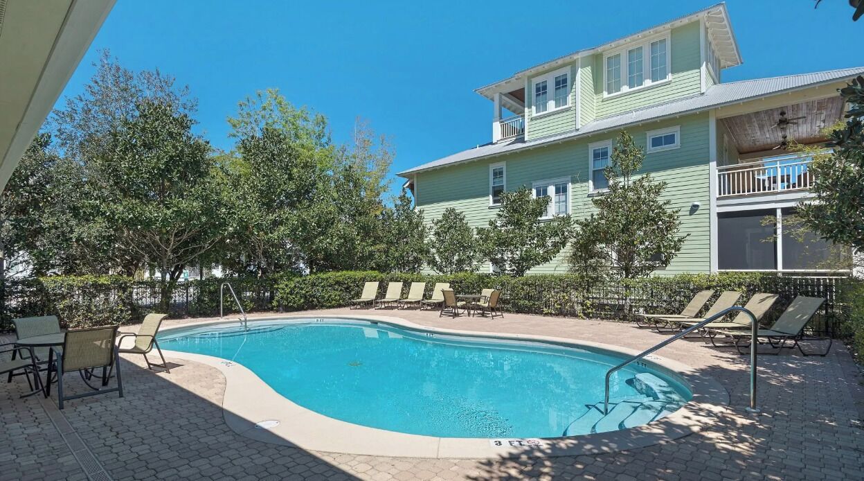 A swimming pool with lounge chairs and a two-story building in the background.