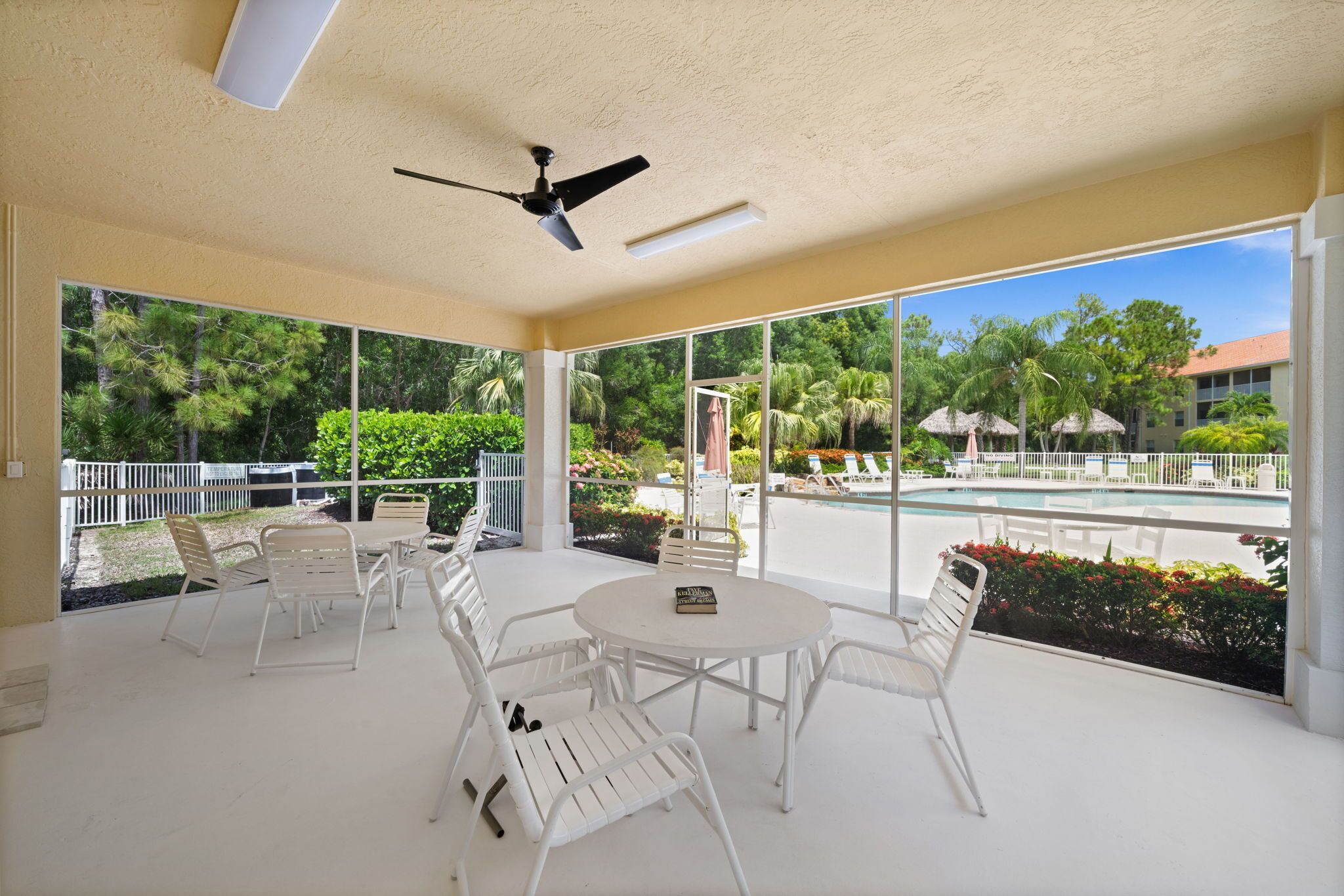 A spacious indoor area with a ceiling fan, large windows, and a pool view.