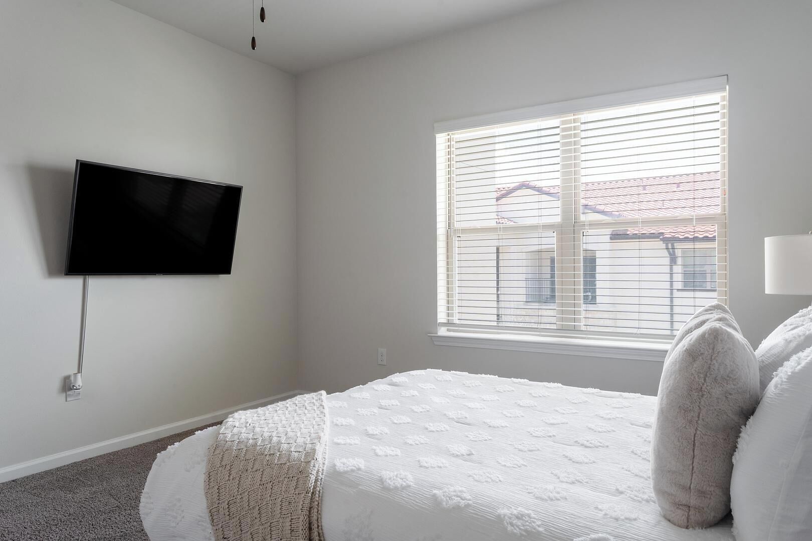 Un dormitorio con una cama, un televisor montado en la pared y una ventana con persianas.