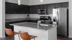 Eine moderne Küche mit dunklen Schränken, einer Arbeitsplatte aus Granit, Edelstahlgeräten und zwei Ledersitzhocker.
