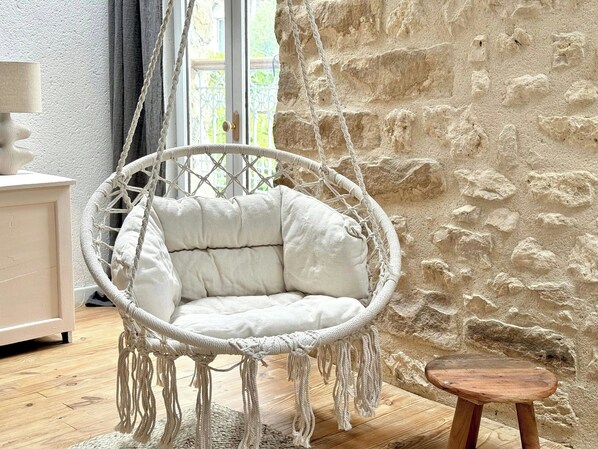 A macrame hanging chair with a cushion, a wooden stool, and a stone wall.