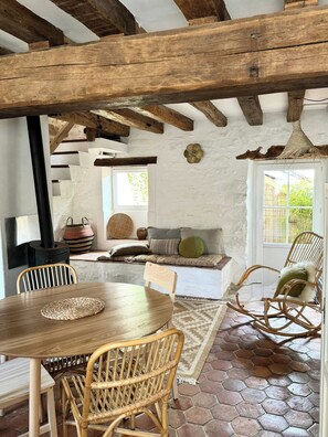 A rustic interior with exposed wooden beams, a stone fireplace, wicker furniture, and a hexagonal tiled floor.