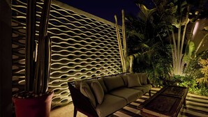Un espacio al aire libre con una pared decorativa, un sofá, una mesa y una planta en maceta.