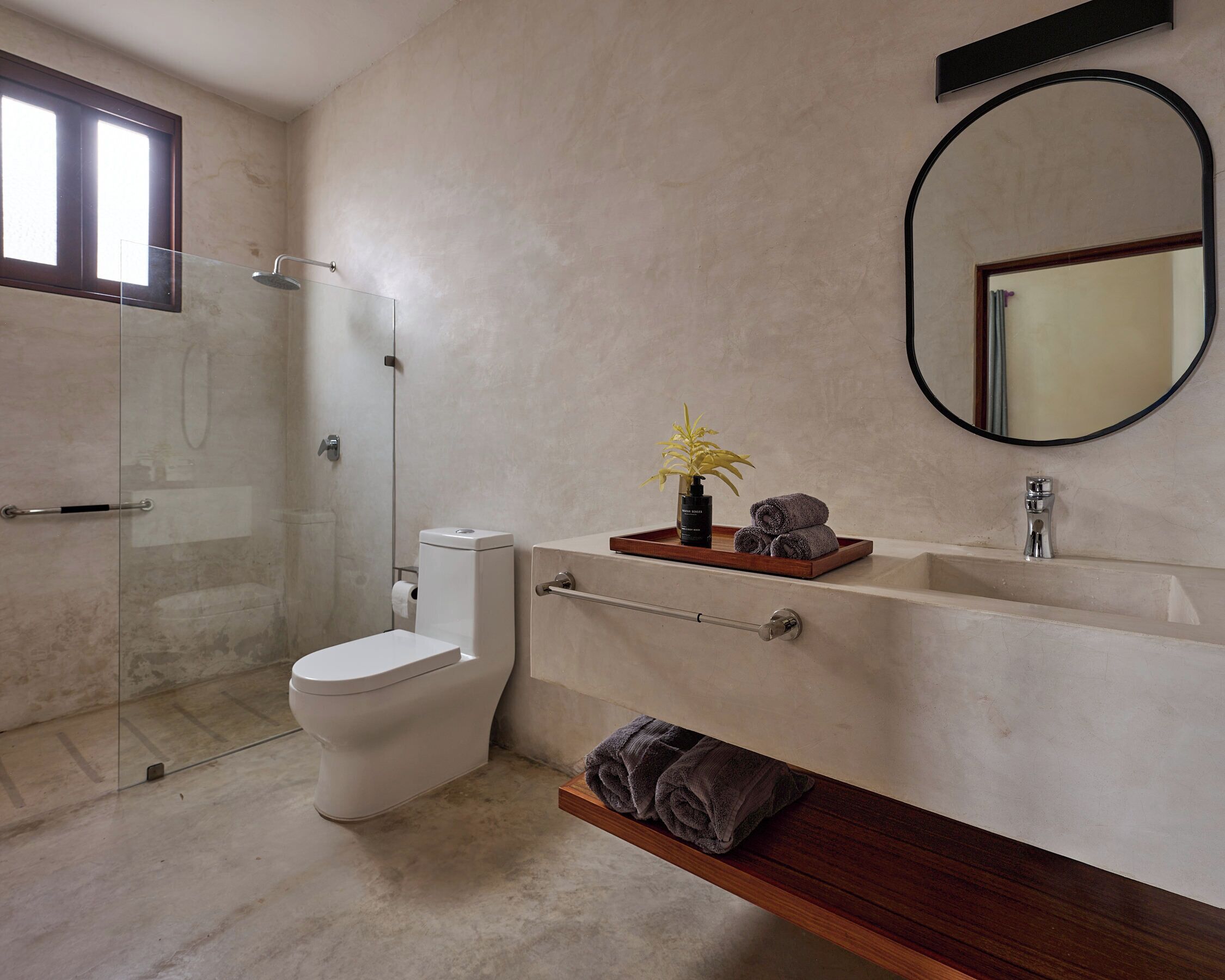 Een moderne badkamer met een glazen douchecabine, een toilet, een wastafel met spiegel en een houten plank met handdoeken.