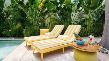 Un espace de détente aménagé au bord de la piscine, avec deux chaises longues à rayures jaunes, une petite table ronde jaune sur laquelle se trouvent un saladier et une carafe, ainsi qu'une petite poubelle jaune.