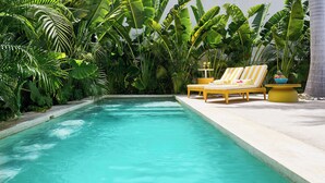 Una piscina con agua turquesa cristalina, rodeada de exuberante vegetación tropical y sillas de descanso amarillas.