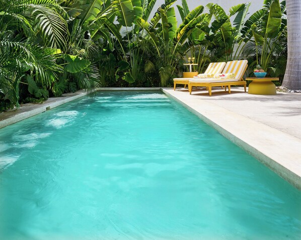 Une piscine à l’eau turquoise et cristalline, entourée d’une végétation tropicale luxuriante et de chaises longues jaunes.