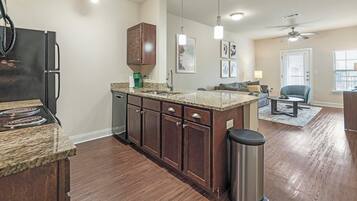 A modern kitchen with granite countertops, dark wooden cabinets, a stainless steel range hood, and a built-in dishwasher.