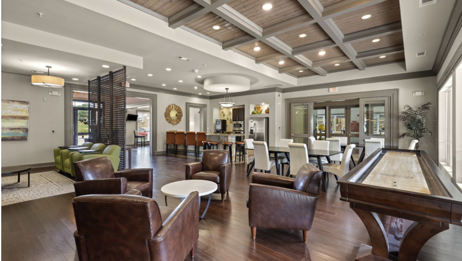 A spacious lobby with leather seating, a billiards table, and a kitchen area in the background.