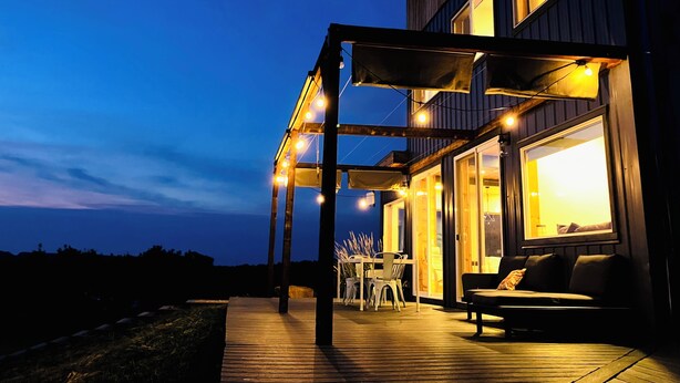 A modern house with a wooden deck, outdoor seating, and string lights.