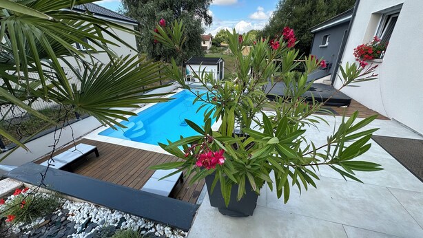 A modern outdoor pool area with a wooden deck, surrounded by potted plants and flowers.