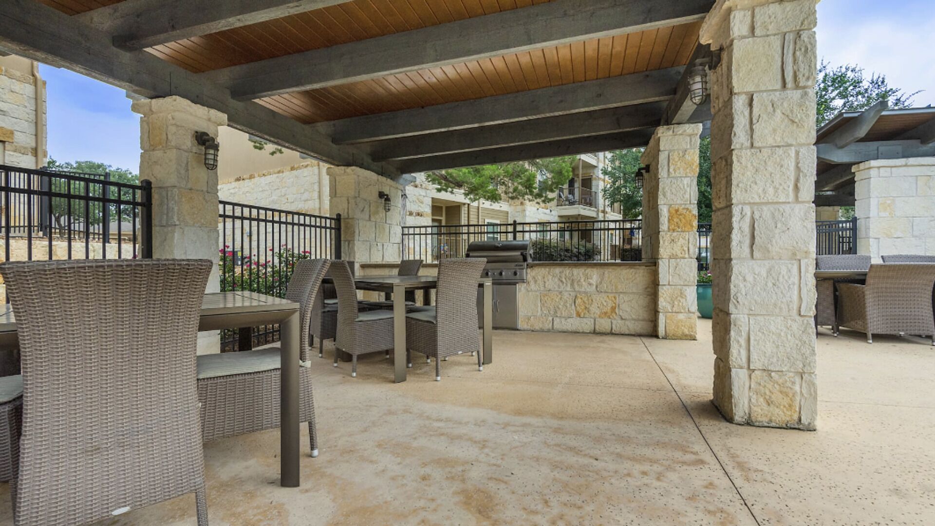 Un espace extérieur aménagé en terrasse, avec des piliers en pierre, des meubles en osier et un barbecue.