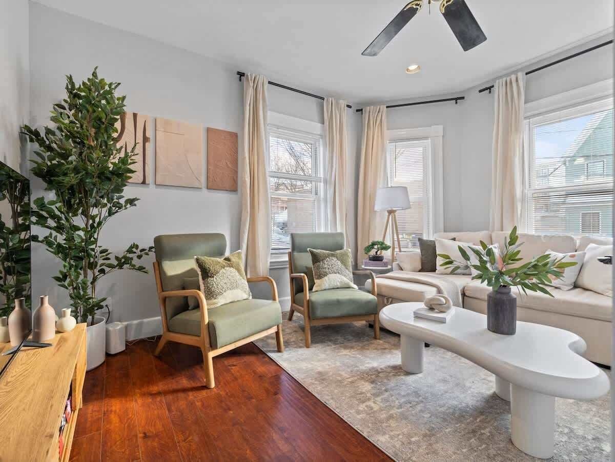 Een moderne woonkamer met een houten vloer, twee groene fauteuils, een witte bank, een bijzettafeltje en een grote plant.
