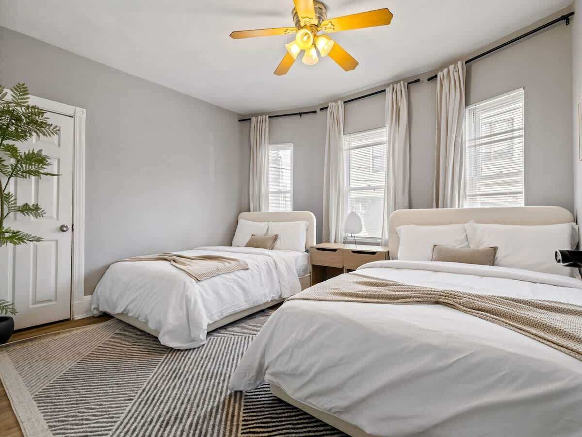 Een slaapkamer met twee bedden, een plafondventilator, een raam met gordijnen en een deur.