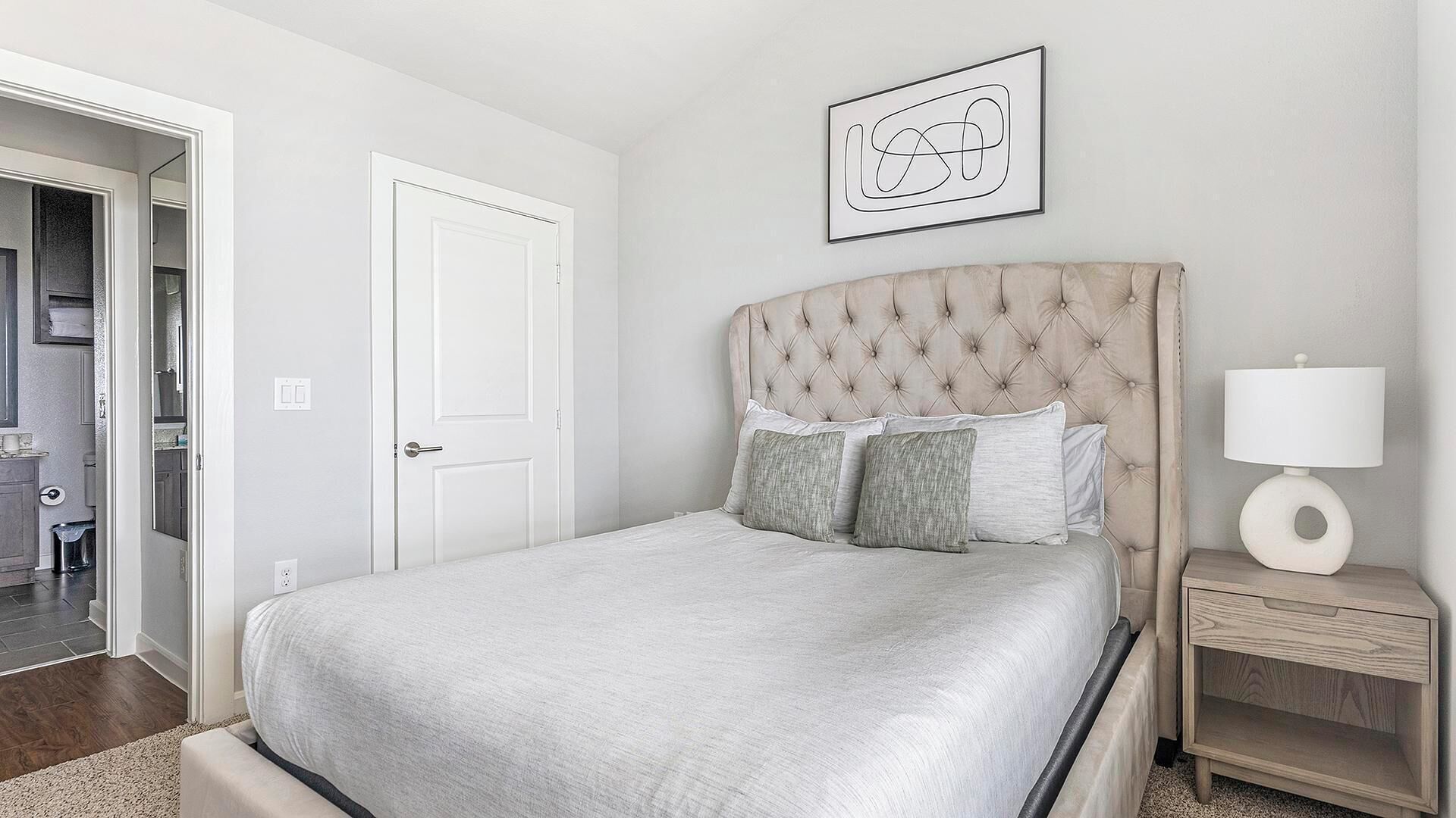A bedroom with a bed, a bedside table, a lamp, and a door.