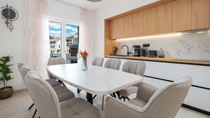 A modern kitchen with wooden cabinets, a marble countertop, and a dining area with a white table and grey chairs.