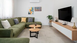 A modern living room with a green sectional sofa, two round wooden tables, a flat-screen TV, and a pendant light.