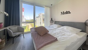 Une chambre d’hôtel avec un grand lit, une chaise, un bureau et une vue sur des immeubles et un phare, visible par la fenêtre.