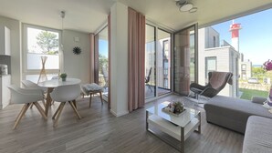 Un salon moderne avec un coin repas, de grandes portes-fenêtres coulissantes donnant sur un balcon et une vue sur un phare.