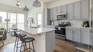 A modern kitchen with grey cabinets, a central island with bar stools, a built-in oven, and a microwave. - Landing | Amazing 1BD, Pool, Clubhouse (Austin)