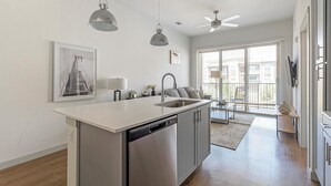A modern kitchen with a dishwasher, a sink, and a ceiling fan. There is a dining area with a table and chairs visible through the window. - Landing | Amazing 1BD, Pool, Clubhouse (Austin)