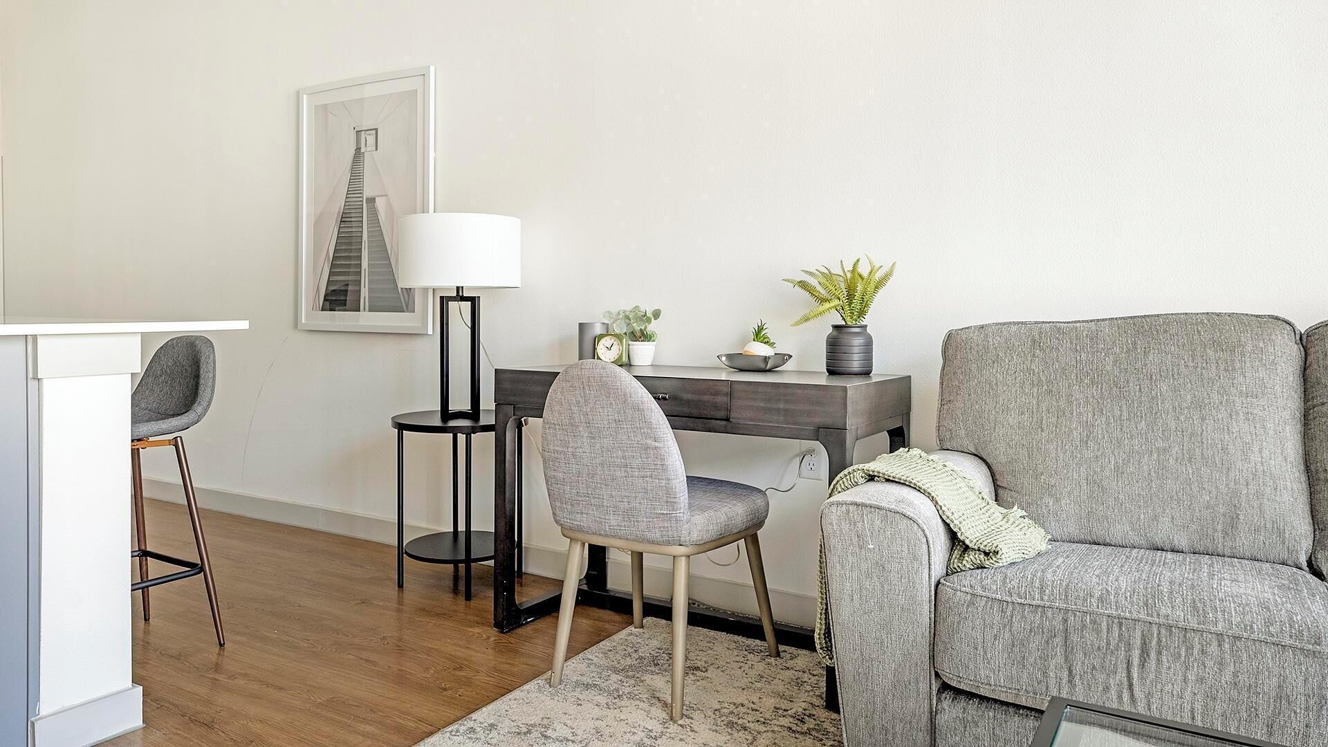 A modern living room with a desk, a grey armchair, a high chair, and a lamp.