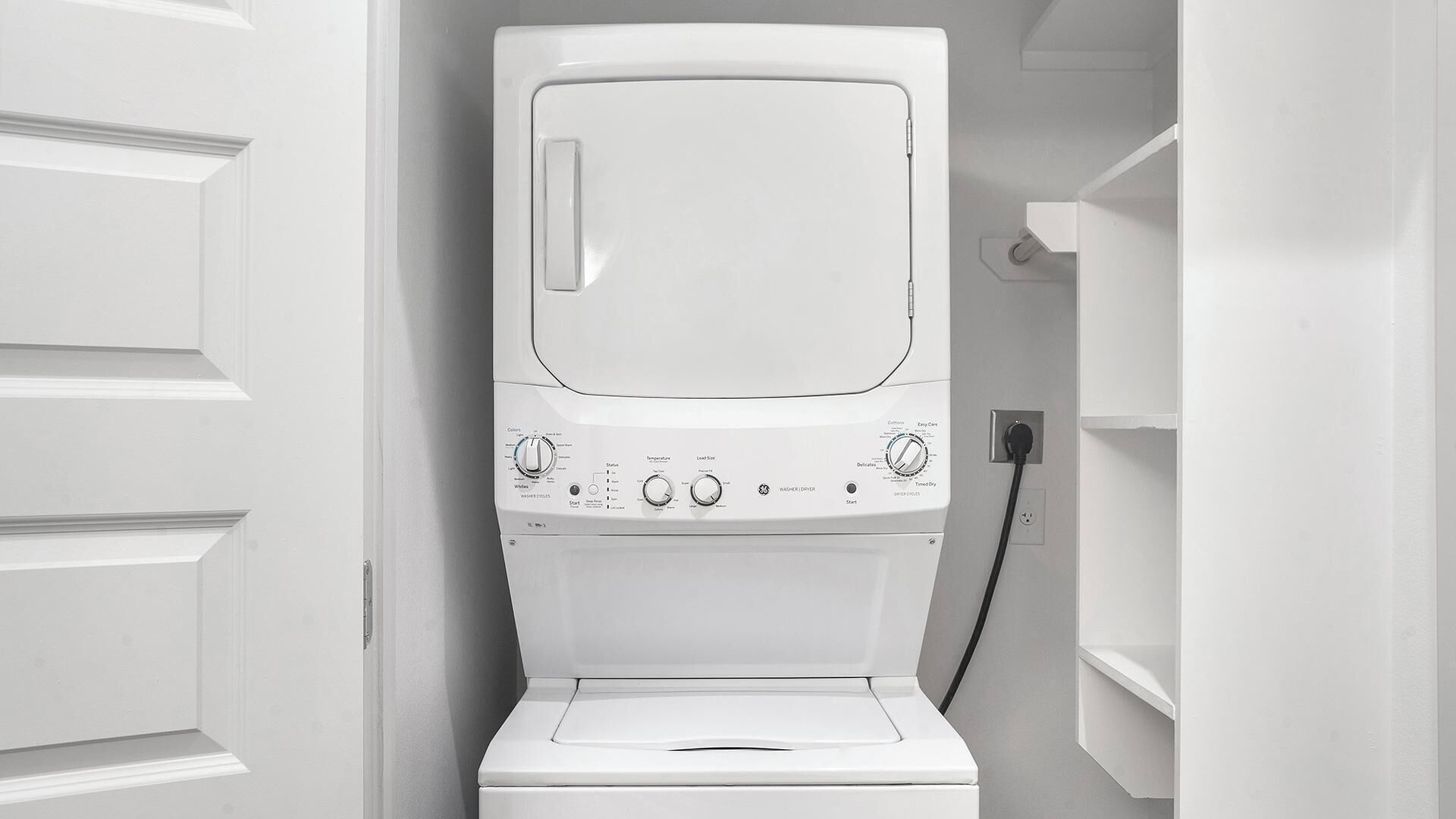 A white washing machine in a laundry room with a door on the left and a shelf on the right.