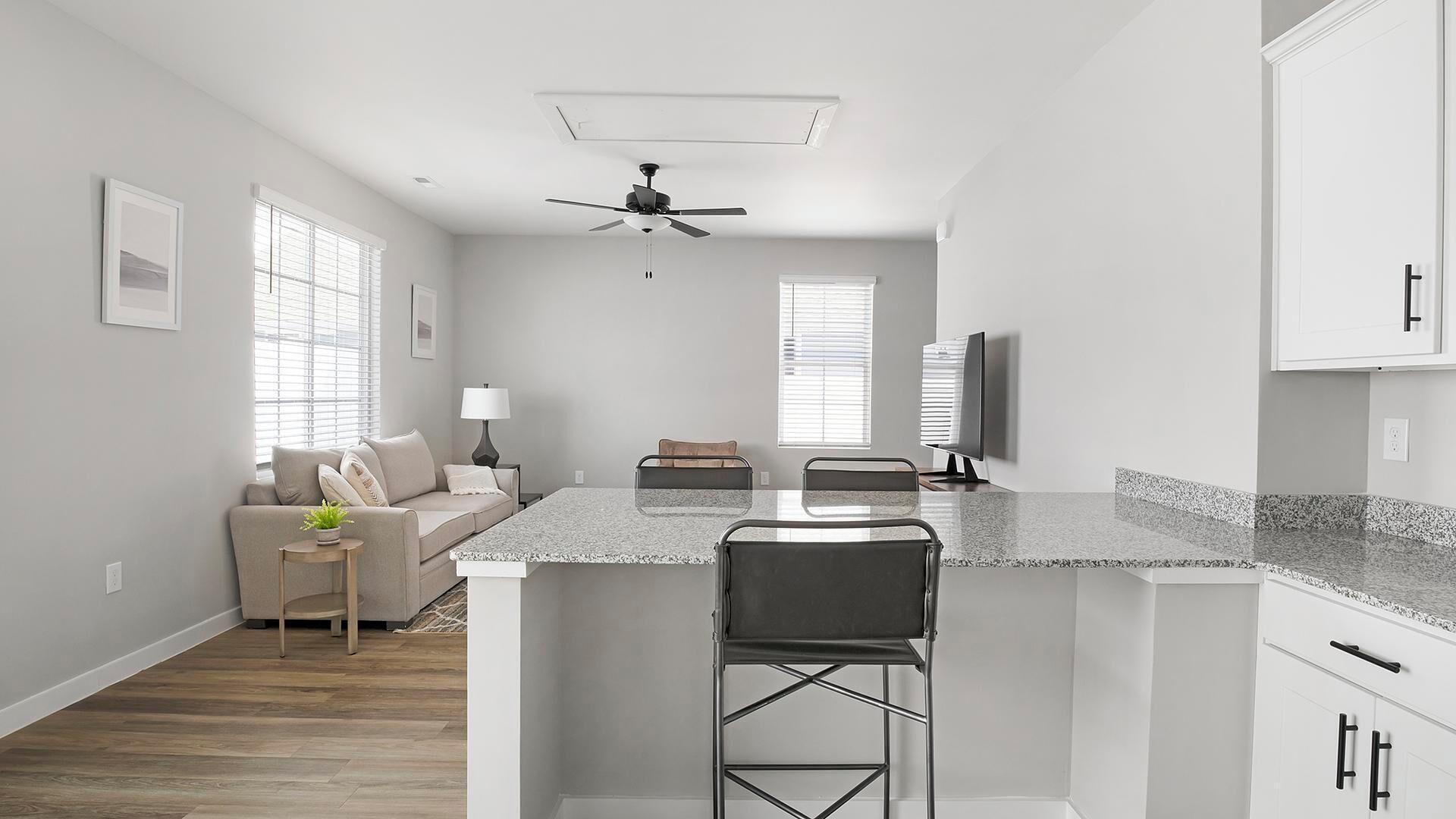 A modern kitchen with a central island, bar stools, a ceiling fan, and a flat-screen TV.