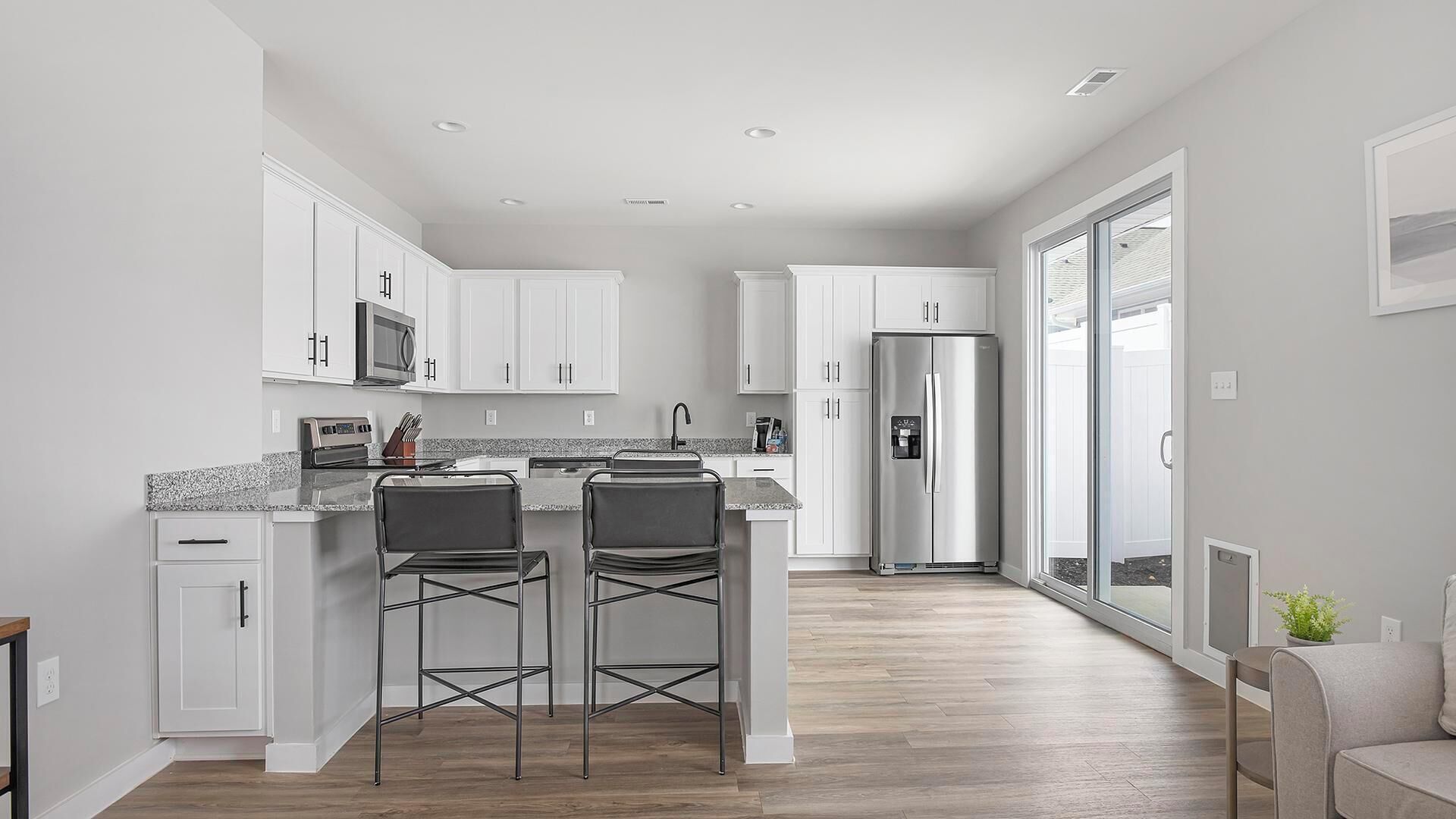 A modern kitchen with white cabinetry, a stainless steel refrigerator, and a bar area with two stools.