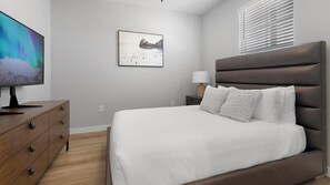 A bedroom with a bed, a TV, a nightstand, a lamp, and a framed picture on the wall. - Landing | Beautiful 1BD, Gym, Pool (Madison)
