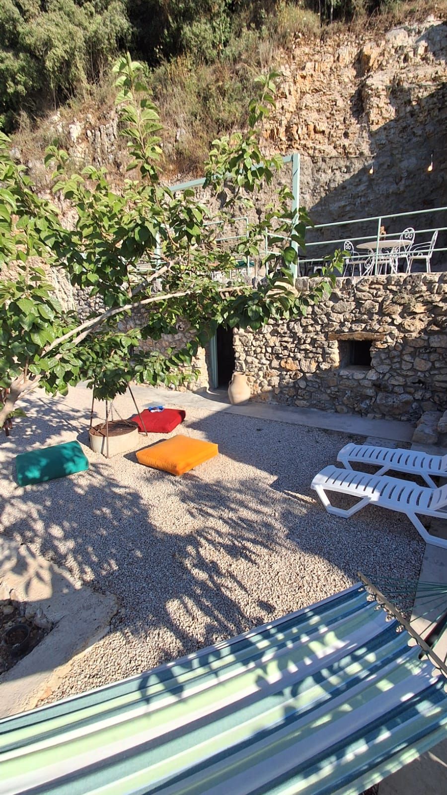 A patio area with outdoor seating, a stone wall, and a tree providing shade.