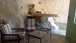 Una habitación acogedora con una pared de piedra rústica, un banco de madera, una silla a rayas y una mesita con tablero estampado.