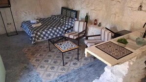 Una habitación rústica con una cama, dos sillas, una mesita y un lavabo.