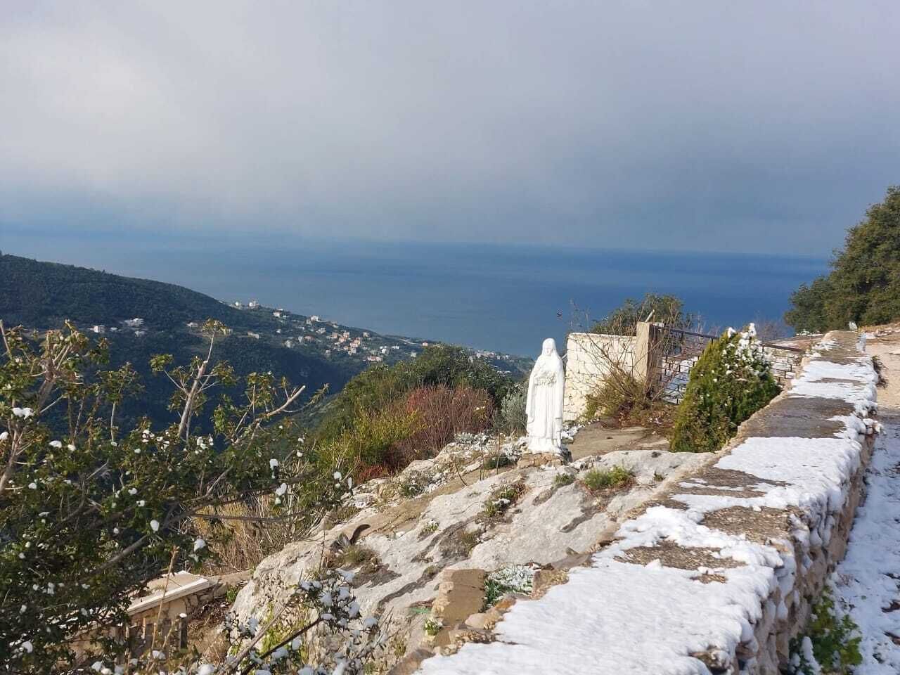 A stone pathway with a statue, overlooking a coastal landscape with distant buildings.