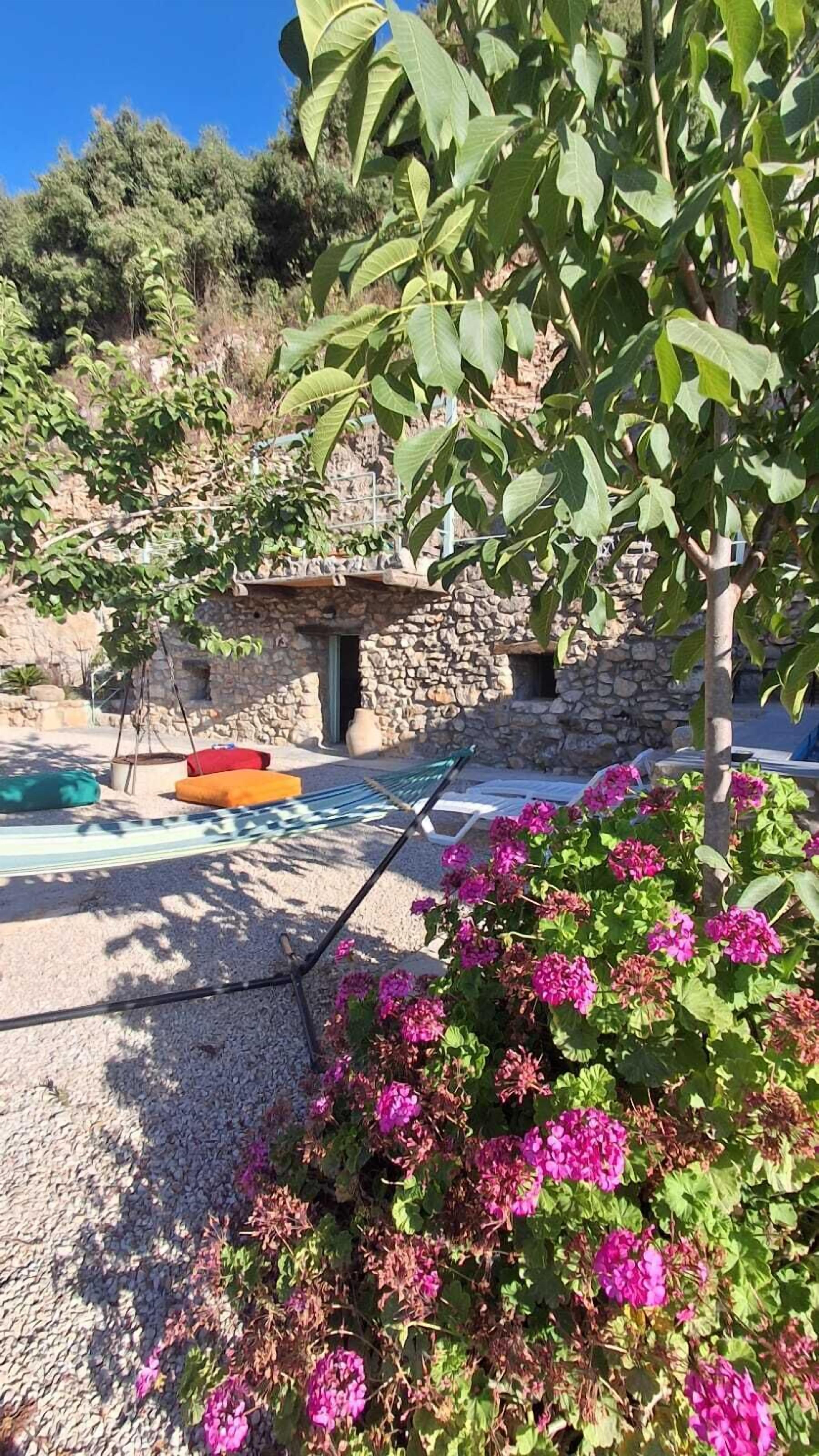 A stone building with a door, a hammock, and colorful cushions.